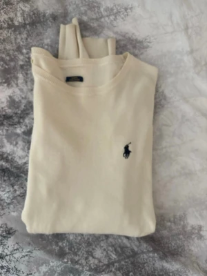 Beige stickad tröja från Polo Ralph Lauren - Snygg beige stickad tröja från Polo Ralph Lauren i slim fit-modell. Tillverkad av mjuk pima bomull och har den klassiska broderade loggan på bröstet. Nypris 2400 kronor, lappen ramlat av, därav rabatterat pris. Storlek M