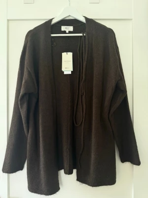 Brun kofta från Gina Tricot, ullmix - Mysig brun kofta från Gina Tricot i ullblandning. Koftan har öppen front och ett knytband i midjan för en avslappnad look. Perfekt lager på lager-plagg med lång ärm och enkel design som passar till det mesta.