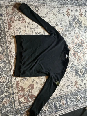 Svart sweatshirt från Stone Island - Säljer en svart sweatshirt från Stone Island med den ikoniska kompassen på vänster ärm. Tröjan har rund halsringning och ribbade muddar vid ärmslut och nederkant. Perfekt för dig som gillar streetwear och vill ha en clean look.