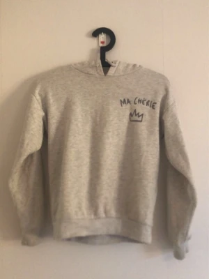 Grå hoodie med tryck Ma Chérie - Ljusgrå hoodie med huva och trycket 'Ma Chérie' samt en krona på bröstet och ryggen. Mjuk och skön, perfekt som snygg men ändå bekväm. Storleken är 134/140 men den känns större.🥰