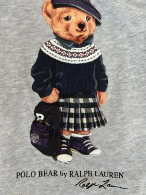 Grå långärmad topp Polo Bear - Grå långärmad topp från Ralph Lauren med Polo Bear-tryck framtill. Trycket visar en björn i rutigt och stickat ”schoolgirl bear”. Väldigt mjuk och bekväm, perfekt till vardags ☺️. Säljer för at jag tyvär inte längre passar i den. 