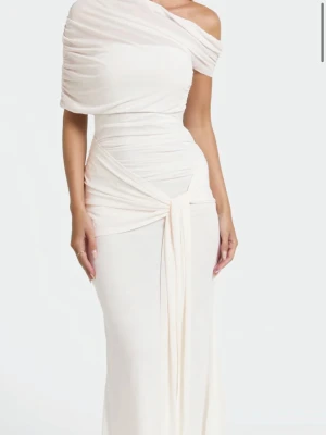 Lång vit omlottklänning offshoulder - Elegant långklänning i vit ton med omlottdetalj och offshoulder-design. Klänningen har draperad överdel och markerad midja med knytband framtill. Perfekt för dig som vill ha en stilren och sofistikerad look. Endast använt i några timmar. Den är en storlek s men passar xs och en mindre m. Nypris 1200kr🤍