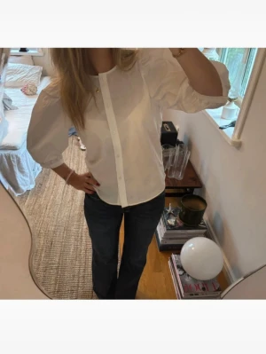 Vit puffärmad blus med knappar - Säljer en vit blus med puffiga korta ärmar och knäppning framtill. Blusen har en rak passform och är tillverkad i ett tunt, lätt material som ger en luftig känsla. Perfekt för en stilren och trendig look. Storlek xs men skulle säga passa xs-s. Aldrig använd så tröjan är i fint skick. 