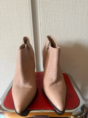 Beige stövletter med klack - Snygga beige stövletter i skinn med spetsig tå och bred klack. Dragkedja på insidan för enkel påtagning. Perfekta för dig som vill ha en stilren och trendig look. Passar till både jeans och kjol.