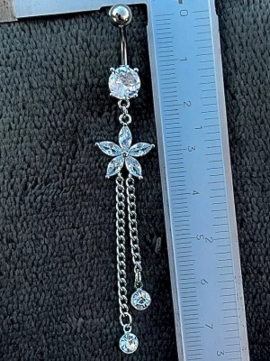 NY oanvänd Navelpiercing med långt hänge | Kirurgiskt stål | Blomma, kedjor och vita stenar  - 💕30% Bundle-rabatt vid köp av minst 2 artiklar. ⭐️NY oanvänd piercing i kirurgiskt stål; rostfritt och säkert för läkta piercingar.                               📏MÅTT ⭕️Stavens längd: 10mm ⭕️Stavens tjocklek: 1,6mm  ⭕️Smyckets totala längd: 80mm                                                                         🤍Färger: Silver och vit                                                            💌Skickas spårbart via Plick SafePay.