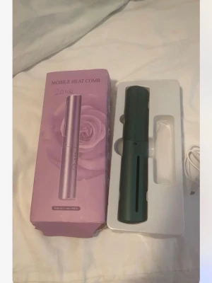 Värmeborste - Säljer en grön mobil värmekam som kommer i originalförpackning. Perfekt för att snabbt styla håret när du är på språng. Laddningsbar via USB och smidig att ta med i väskan. Modern design med enkel knappstyrning.