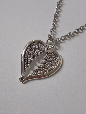 Halsband med hjärta och vingar i silverfärg - Snyggt halsband med ett hjärtformat hänge i silverfärgad metall. Hänget har detaljerade änglavingar som bildar ett hjärta. Kedjan är tunn och matchar hängets färg. Perfekt accessoar för dig som gillar unika smycken med symbolik. Materialet rostfritt stål.