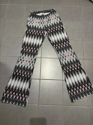 Mönstrade leggings från KappAhl - Säljer ett par snygga leggings från KappAhl med svart, vitt och rosa zigzag-mönster. De har utsvängda ben och resår i midjan för skön passform. Perfekta för dig som gillar färg och mönster! Materialet är mjukt och stretchigt.