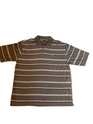 Randig pikétröja från Lacoste - Säljer en grå pikétröja från Lacoste med klassisk krage och knappar framtill. Tröjan har horisontella ränder i beige, vit och vinröd samt den ikoniska krokodilloggan på bröstet. Perfekt för en avslappnad men ändå stilren look.