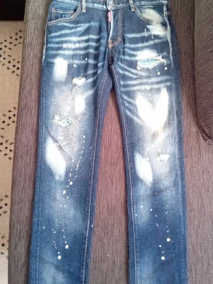 Dsquared - Säljer ett par blå jeans med slitna detaljer, färgstänk och tryck på bakfickan. Jeansen har raka ben, fem fickor och coola slitningar framtill. Perfekta för dig som gillar en streetwear-look.