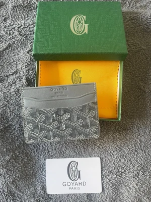 Grå G-korthållare - Snyggt grått kortfodral med mönster i vitt och grått. Fodralet har flera kortfack och är tillverkat i exklusivt läder med tryck. Perfekt för dig som vill ha en stilren och lyxig accessoar.