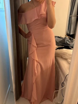 Rosa balklänning med volang - En superfin rosa långklänning med en axel och volangdetaljer längs överdelen och sidan. Klänningen har oneshoulder-design och är figurnära med fina volanger och slits i benet. Perfekt för speciella tillfällen, tex till bal i skolan. Från JJ’s house, orginalpris 2000 och endast använd typ 2 gånger.