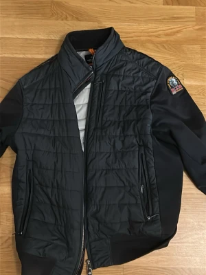 Svart quiltad jacka från Parajumpers - Snygg svart quiltad jacka från Parajumpers med hög krage och dragkedja framtill. Jackan har två fickor med dragkedja och ett patchmärke på ärmen. Perfekt för dig som vill ha en stilren och funktionell jacka.
