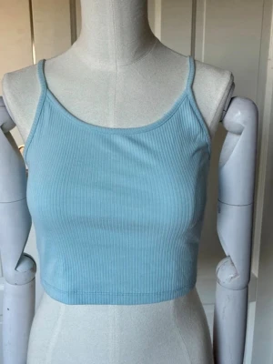 Ljusblå ribbad crop top - Säljer en ljusblå ribbad crop top med tunna axelband. Toppen har en tight passform och är tillverkad i ett stretchigt material som sitter bekvämt mot kroppen. Säljer pga att den inte används och storleken kan upplevas som xs/s/m💓
