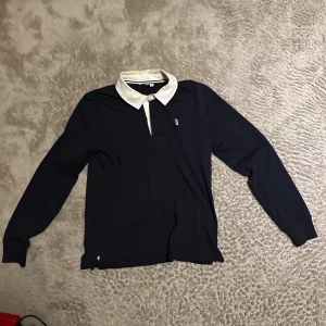 Marinblå långärmad skjorta med vit krage - Marinblå långärmad skjorta med kontrasterande vit krage och knappdetalj framtill. Klassisk och stilren design som passar till många olika looks. Skjortan har en rak passform och är tillverkad i ett mjukt material.