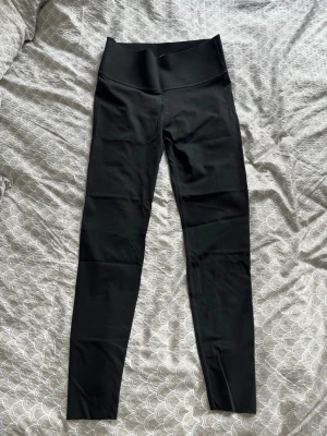 Svarta höga leggings - Säljer ett par svarta leggings med hög midja och tight passform. De är tillverkade i ett stretchigt material som sitter skönt mot kroppen och passar perfekt till en avslappnad eller sportig stil. Inga synliga loggor eller detaljer. Passar bra att använda vid träning 