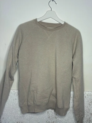 Beige sweatshirt med rund hals - En enkel beige sweatshirt med rund halsringning och ribbade muddar vid ärmar och nederkant. Tröjan har en avslappnad passform och är tillverkad i mjukt bomullsmaterial. Perfekt för en casual och stilren look.