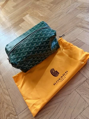 Grön necessär  - Snygg grön necessär med klassiskt mönster i vitt och grått. Kommer med original gul dustbag. Perfekt för att organisera dina essentials. Helt ny, pris kan diskuteras