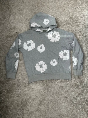 Grå denim tears hoodie - Snygg grå denim tears hoodie med vita blommönster över hela tröjan. Hoodien har en klassisk huva och ribbade muddar vid ärmar och nederkant. Perfekt för en avslappnad och trendig look. Tillverkad i mjukt sweatshirtmaterial för extra komfort. Passar perfket med de matchande byxorna. Hela settet/tracksuiten finns i min profil som en egen annons.