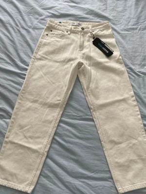 Vita raka jeans från Above Now - Säljer ett par vita jeans från Above Now med rak passform och klassisk femficksdesign. Jeansen har hög midja och är tillverkade i ett kraftigt bomullstyg. Perfekta för dig som gillar en clean och stilren look.