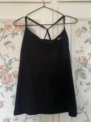Svart linnetopp från Nike - Snygg svart linnetopp från Nike med tunna axelband och ett sportigt snitt. Matrialet är mer sportigt tyg och ryggen är ganska luftig. Skriv om ni har funderingar🩷