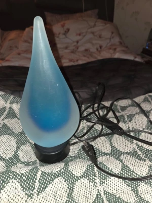 Blå droppformad bordslampa - Säljer en unik bordslampa i frostat blått glas med droppformad design. Lampan har svart fot och medföljer sladd för ström. Perfekt som mysbelysning eller dekoration i rummet.