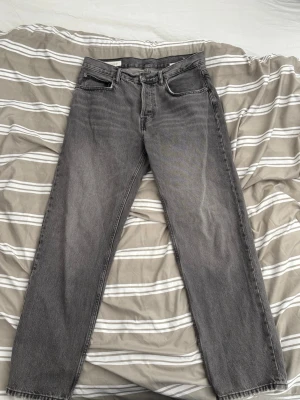 Grå raka jeans från Zara - Säljer ett par grå jeans med rak passform och klassisk femficksdesign. Jeansen har en snygg tvättad look och är tillverkade i kraftigt denimtyg. Perfekta för dig som gillar en avslappnad och tidlös stil.