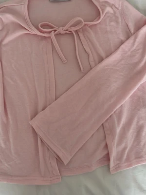 Ljusrosa cardigan med rosett - Söt ljusrosa cardigan från 157 med lång ärm och en fin rosettknut vid halsen. Pris kan diskuteras pga frakt. Använd max 3 gånger.