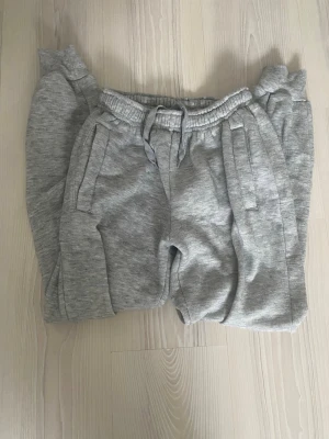 Grå mjukisbyxor från Vega - Säljer ett par grå mjukisbyxor från Vega med dragsko i midjan och resår. Byxorna har två sidofickor och är gjorda i mjukt, fleeceliknande material. Perfekta för chill dagar eller när du vill vara extra bekväm. Jättemjuka!