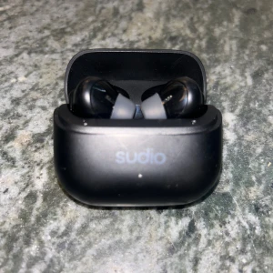 Sudio svarta trådlösa in-ear hörlurar - Snygga svarta trådlösa in-ear hörlurar från Sudio med matchande laddningsetui. Hörlurarna har en stilren och kompakt design i matt plast och passar perfekt för musik, poddar och samtal på språng.