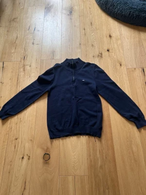 Mörkblå halvzip-tröja från Lexington - Snygg mörkblå stickad tröja från Lexington med halvzip och ståkrage. Tröjan har ribbade muddar vid ärmslut och nederkant samt en liten Lexington-logga på bröstet. Perfekt för dig som gillar klassisk och stilren design.