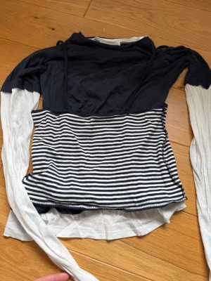 Randig långärmad topp i blått och vitt - Trendig långärmad topp med marinblå överdel och vita ärmar. Nedre delen har ett klassiskt blåvitt randigt mönster. Toppen har en smal passform och är tillverkad i mjuk bomull, perfekt för en avslappnad men stilsäker look.