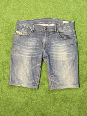 Blå jeansshorts från Diesel - Snygga blå jeansshorts från Diesel med klassisk femficksdesign och uppvikta benslut. Shortsen har en avslappnad passform och är tillverkade i slitstark bomull. Perfekta för sommardagar och enkel att matcha med t-shirt eller hoodie.