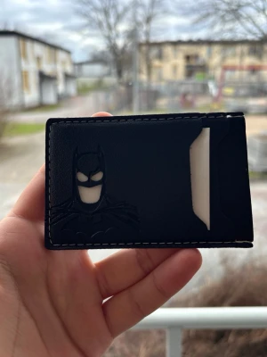 Svart Batman kortfodral i läder - Säljer ett svart kortfodral i läder med Batman-motiv präglat på framsidan. Fodralet har vita sömmar runt kanterna och ett fack för kort. Perfekt för dig som gillar superhjältar och vill ha något stilrent och unikt i fickan.
