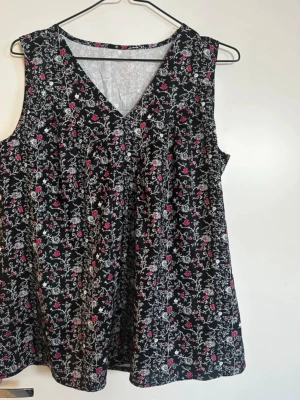 Blommig ärmlös linnetopp svart - Snygg ärmlös linnetopp med svart botten och blommigt mönster i vitt och rosa. Toppen har v-ringning och en lös passform som ger en avslappnad vibe. Perfekt för varma dagar och enkel att styla med jeans eller kjol. Rök och djurfritt hem. Pruta gärna !🌸