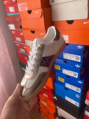 Tamaris sneakers med leoparddetalj - Snygga vita sneakers från Gola med metallic guld på tån och hälen, samt leopardmönstrad detalj på sidan. Skon har vit ovandel i läder, vita skosnören och en klassisk gummisula. Perfekt för dig som vill sticka ut med coola detaljer.