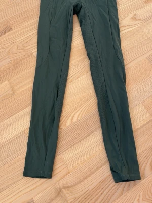 Mörkgröna ridleggings från Horze - Snygga mörkgröna ridleggings från Horze med smal passform och stretchigt material. Perfekta för dig som gillar en sportig look och vill ha bekväma byxor till vardags. Midjehög modell och diskreta sömmar och grepp längs benen.