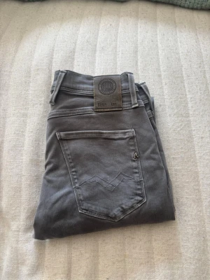Gråa Replay jeans med stretch - Snygga gråa jeans från Replay med klassisk femficksmodell och diskret broderad detalj på bakfickan. Jeansen har stretchigt material för extra komfort och passform. Märkespatch bak i midjan och Replay-logga på fickan. Perfekta till en avslappnad stil.