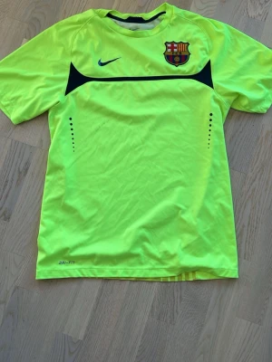 FC Barcelona träningströja Nike 2009/2010 köpt i Barca - Säljer en neongul träningströja från Nike med FC Barcelona-emblem på bröstet. Tröjan har korta ärmar, rund hals och svarta detaljer. Tillverkad i Dri-FIT-material som andas, perfekt för intensiva träningspass eller match. KÖPT I BARCA, fläcken på tröjan är en autograf av legendaren Makelele men som tyvärr har börjat försvinna helt för kännedom.