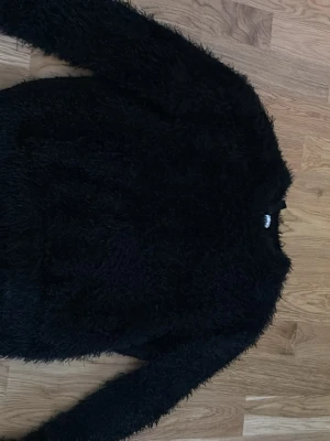 Svart fluffig stickad tröja Divided - Mysig svart stickad tröja från Divided med fluffig textur. Tröjan har rund halsringning och långa ärmar, perfekt för dig som gillar en trendig och bekväm look. Passar till många olika stilar och är enkel att matcha med jeans eller kjol.