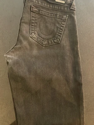 Svarta skinny jeans från True Religion - Säljer ett par svarta skinny jeans från True Religion med klassisk hästsko-detalj på bakfickan. Jeansen har fem fickor, låg midja och är tillverkade i stretchigt denim för en bekväm passform. Perfekta till en avslappnad streetstyle-look.