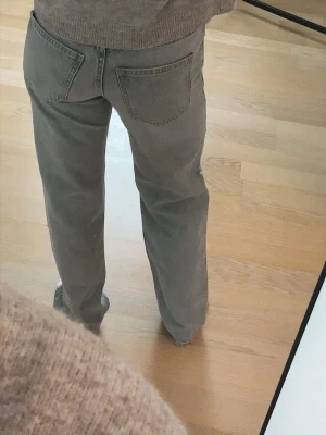 Grå raka jeans med mid midja - Säljer ett par grå jeans med rak passform och hög midja. Jeansen har klassiska fem fickor och bälteshällor. Materialet är denim i bomull och färgen är en snygg tvättad grå. Perfekta för en avslappnad och trendig look.
