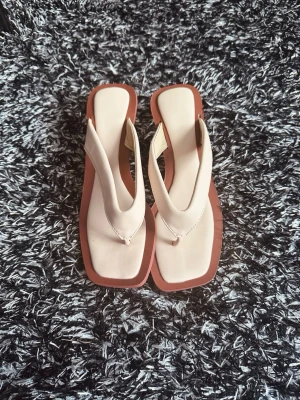 Beige sandaler med klack och fyrkantig tå - Trendiga sandaler i beige med breda remmar och fyrkantig tå. Sulan är brun och klacken är transparent och rundad, vilket ger en modern look. Perfekta för dig som gillar stilrena detaljer och vill sticka ut lite extra. Materialet ser ut att vara konstläder.