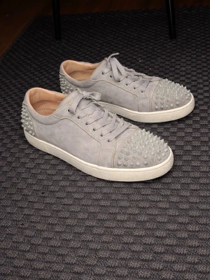 Grå Christian Louboutin skor  - Säljer ett par grå Christian Louboutins  i mocka med coola spikar på tån och hälen. Skorna har snörning och en klassisk platt sula. Insidan är beige och designen är riktigt edgy och unik. Perfekta för dig som vill sticka ut med din stil. Jätte feta men tyvärr saknar 4 spikar därav priset!  (Helt äkta)