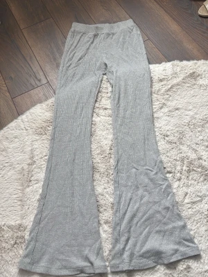 Grå ribbade utsvängda leggings - Säljer ett par grå leggings med ribbad struktur och utsvängda ben. De har hög midja och är gjorda i ett mjukt, stretchigt material som sitter skönt på kroppen. Perfekta för en avslappnad och trendig look.
