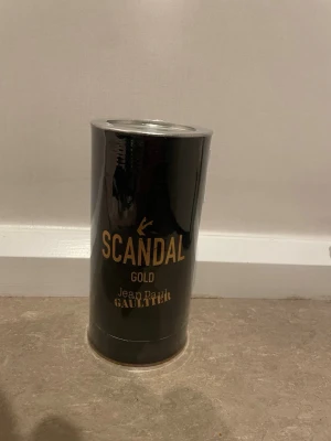 Scandal Gold parfym Jean Paul Gaultier - (80 ml) Scandal Gold parfym från Jean Paul Gaultier i en elegant svart och guld cylinderformad förpackning. Förpackningen har en lyxig metallisk finish och tydlig logga i guld. Perfekt för dig som gillar exklusiva dofter och snygg design.
