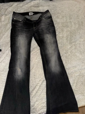 Svarta bootcut jeans med slitningar - Säljer ett par svarta bootcut jeans med snygga slitningar och ljusa tvättade partier på låren. Jeansen har låg midja och klassisk femficksmodell. Perfekta för dig som gillar en retro och avslappnad stil.