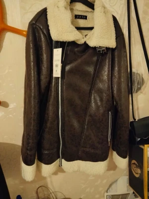 Brun teddyjacka med fuskpäls - Snygg brun teddyjacka från Zara med vit fuskpäls på krage, ärmslut och nederkant. Jackan har en asymmetrisk dragkedja, två fickor med dragkedja och coolt bältesspänne vid halsen. Perfekt för dig som vill ha en trendig och varm look.