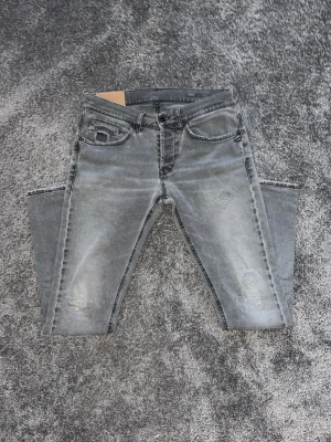 Grå slitna jeans från Dondup  - Säljer ett par grå jeans från Dondup med slitningar och tvättad look. Jeansen har fem fickor, Klassiska Dondup bakfickorna och slim-fit passform. Materialet är denim med en mjuk känsla och cool streetstil.