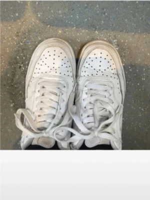 Vita sneakers - Fräscha vita Nike sneakers med klassisk låg siluett. Skorna har perforerad tå, snörning och platt sula. Tillverkade i skinn med diskret Nike-logga på hälen. Perfekta för dig som gillar clean och tidlös streetstil.